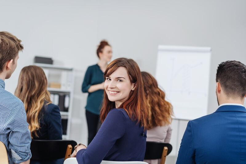 Lernen macht selbstbewusst. In der Ausbildung zum Lerncoach wächst nicht nur dein Wissen – sondern auch dein Selbstvertrauen. Teilnehmerin lächelt in einem Seminar zurück zur Kamera – Freude an Weiterbildung und Austausch